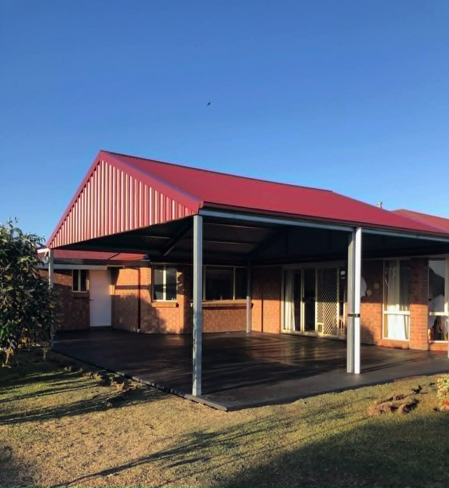 Attached verandah and outdoor living area with red roof by Trevarth Garages
